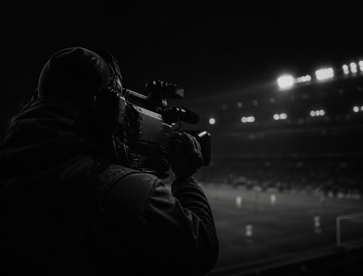 Cinegrafista com câmera de ombro cobrindo uma partida noturna de futebol